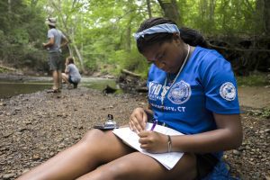 high school student sitting with a notebook by the Fenton River