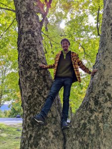 Samuel Kocurek standing in between two tree trunks with green leaves behind him