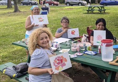 group of women with paintings sitting outside at picnic table