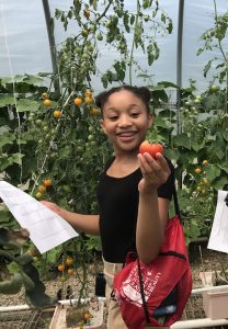 girl with a red string backpack holding paper and tomato