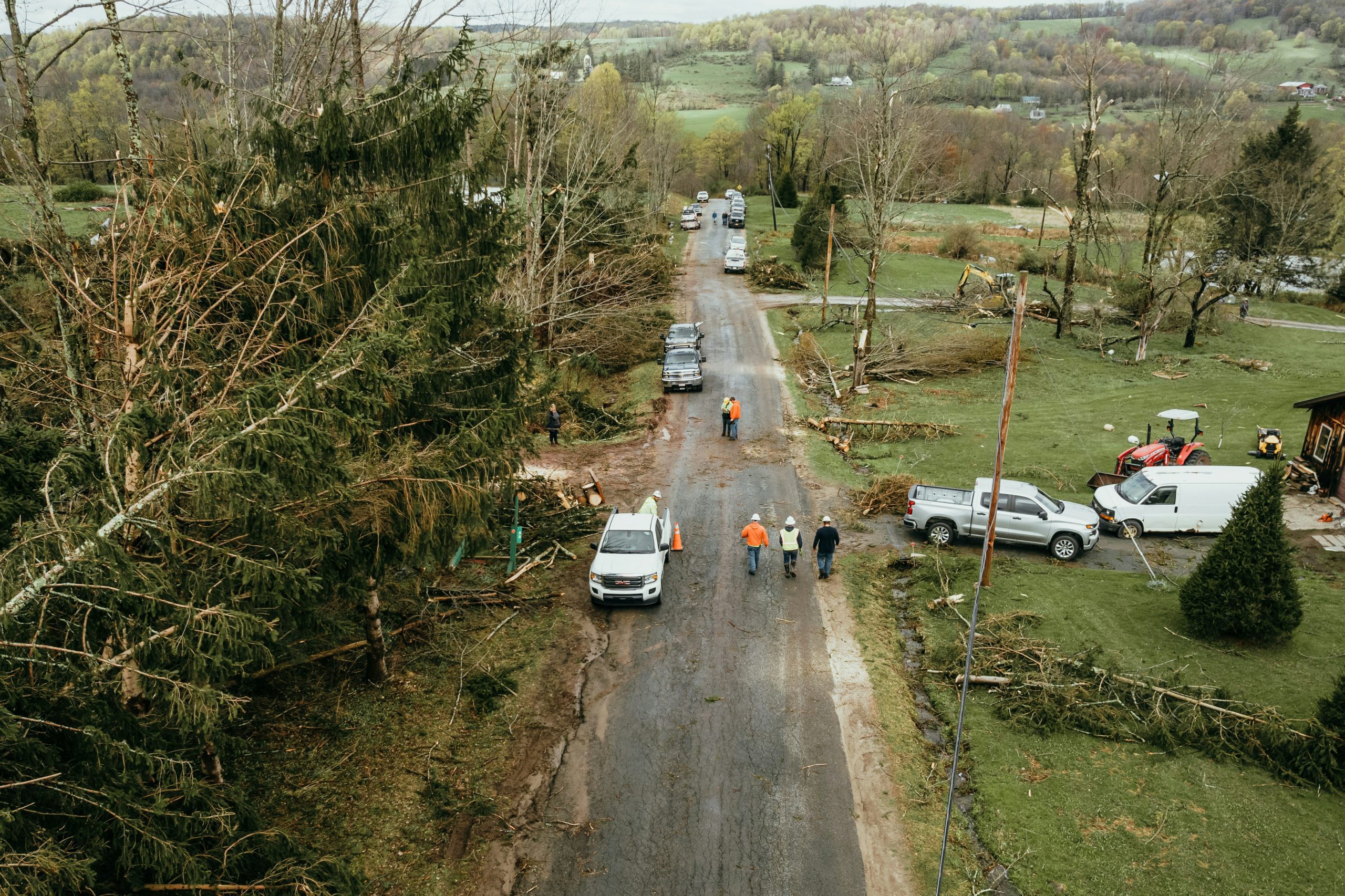 trees and power lines down along a road after a storm with trucks and people in hard hats inspecting the damage