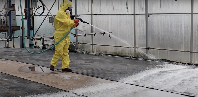 person in a yellow suit spraying foam in a greenhouse