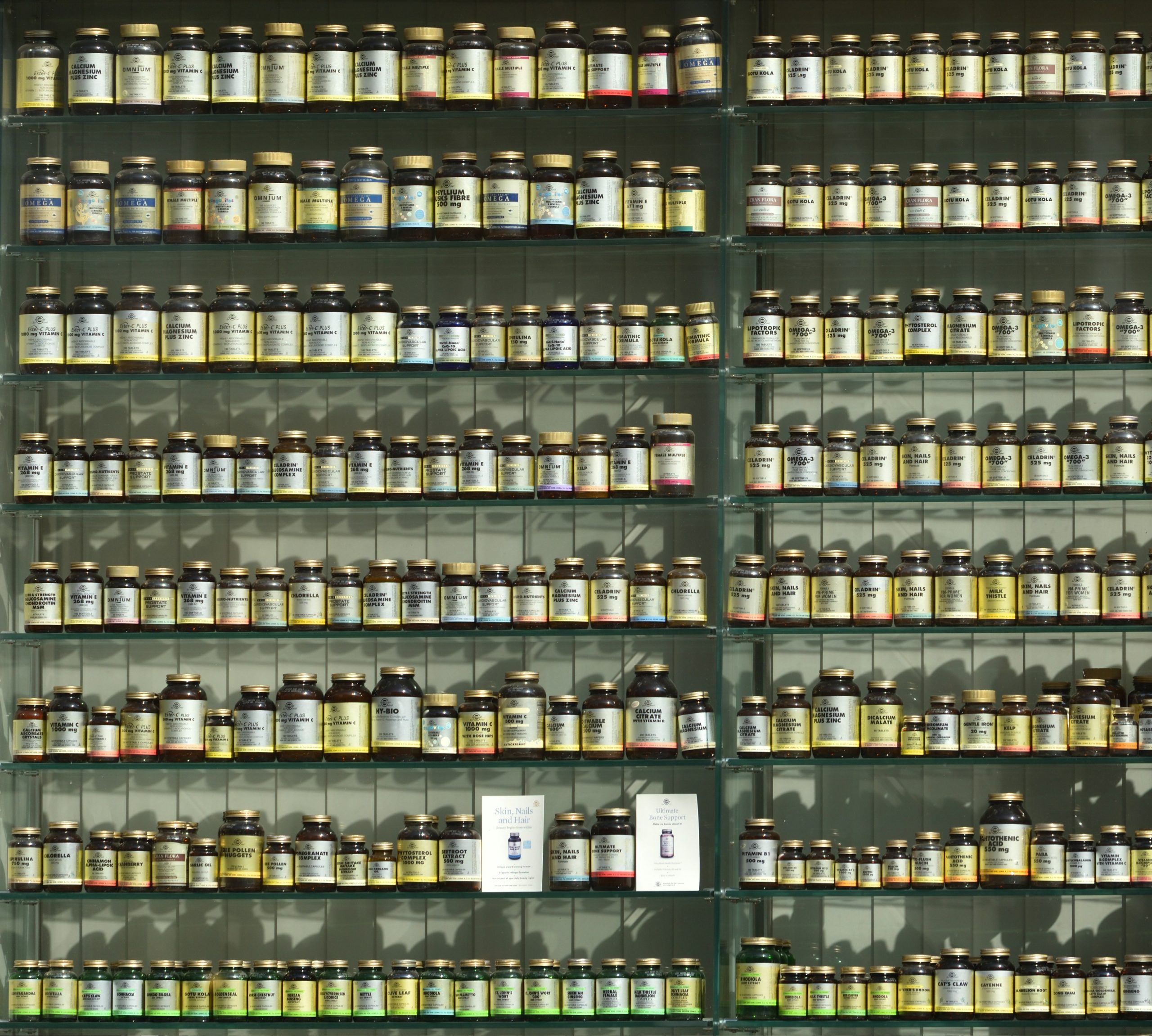A collection of various sized glass bottles of vitamins and supplements on shelves.