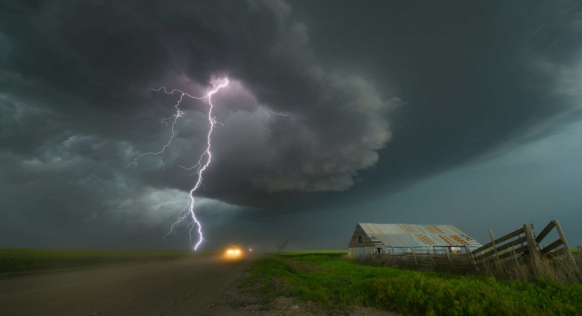 An image of a purple bolt of lightning striking the field on a farm with a wooden fence and metal barn on the right side of the image.