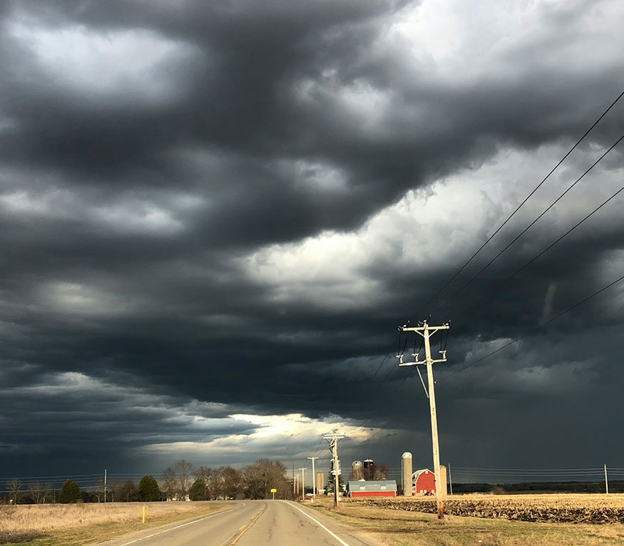 storm clouds over a rural road and a red barn