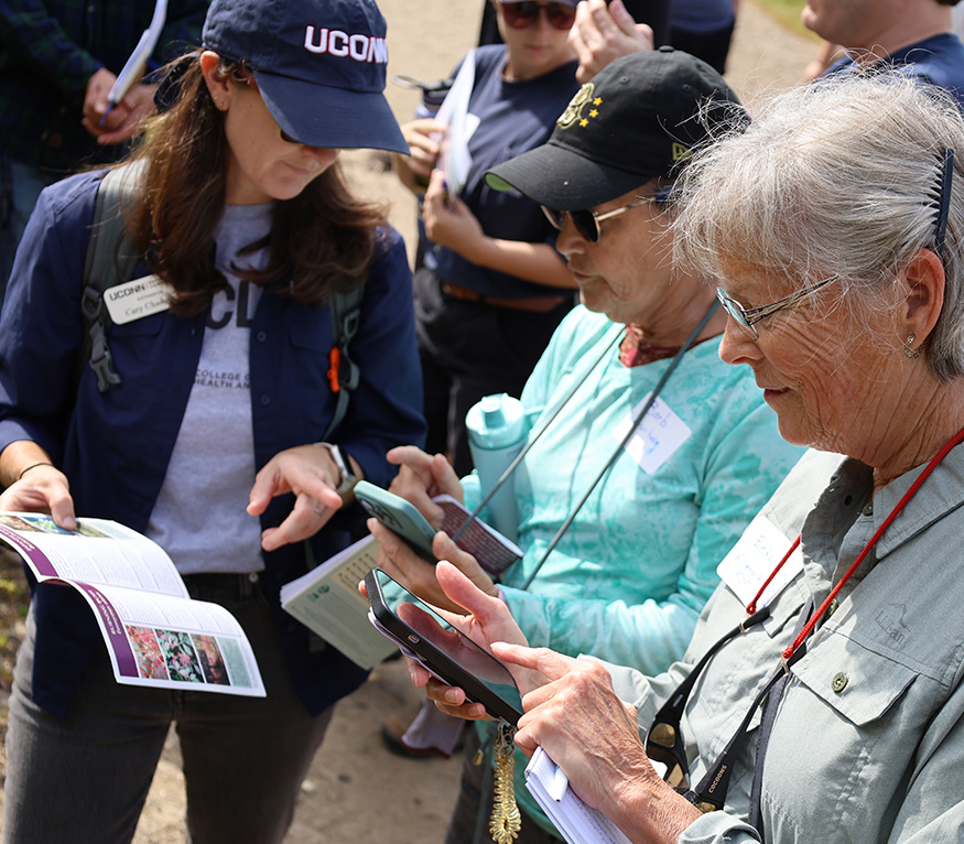 Extension educator shows invasive species list on phone to two women