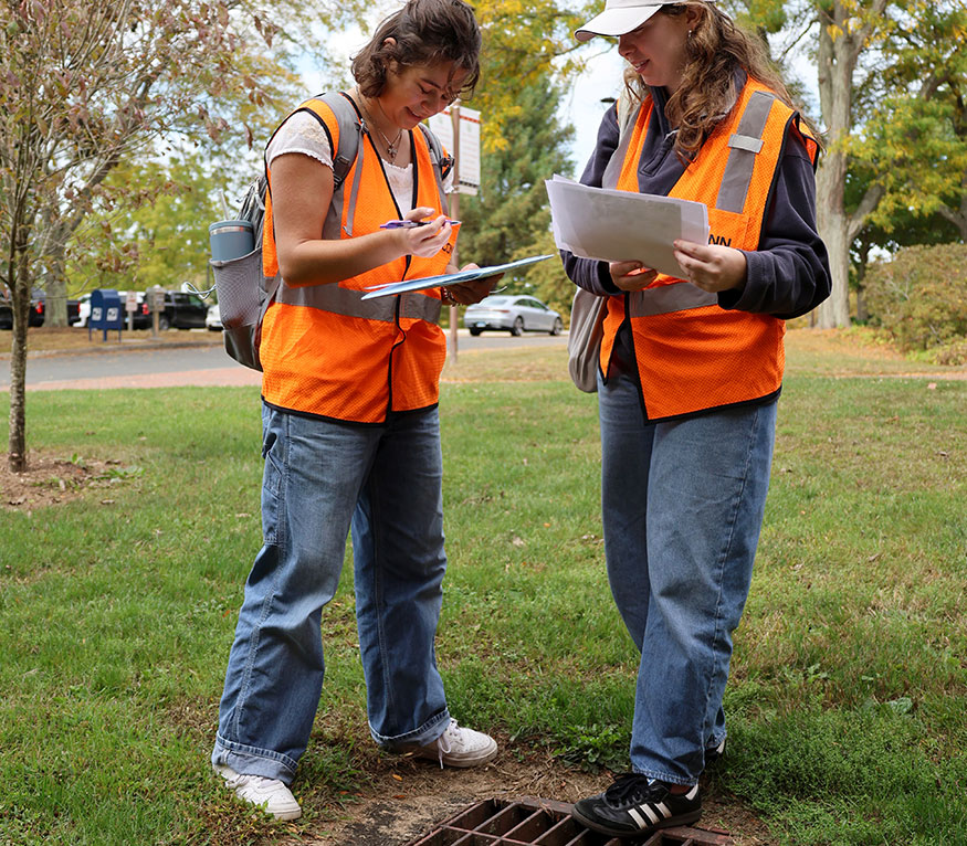 two students taking notes next to a stormdrain.