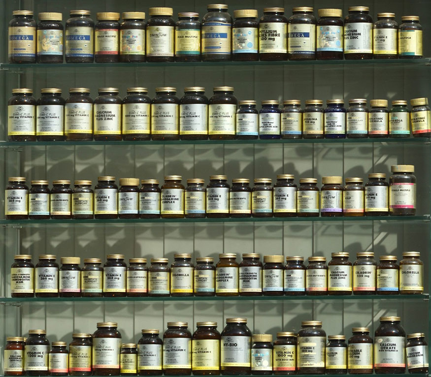 A collection of various sized glass bottles of vitamins and supplements on shelves.