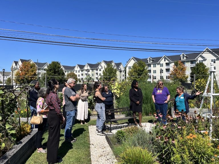 group of people standing in a garden with a woman pointing at plants