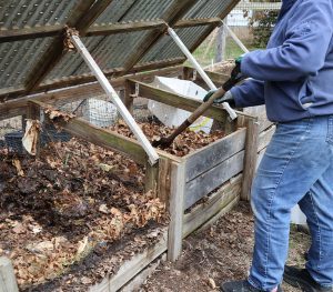 A person turning their compost pile with a shovel.