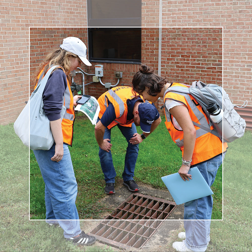 two students and an educator looking down a storm drain.