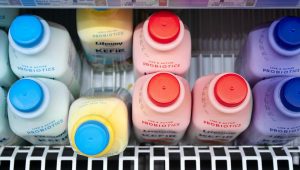 Two rows of blue, yellow, pink, and purple yougurt drink bottles, with a small expiration date printed on the side.