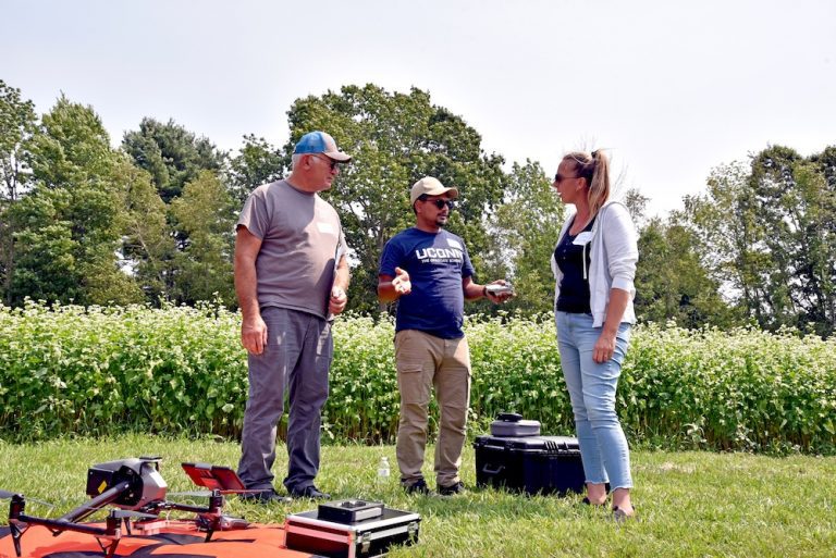 three people talking in a field with crops in the background and a drone in the foreground