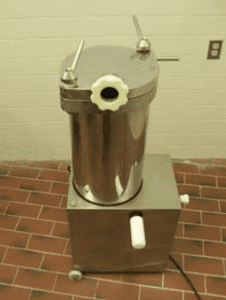 The front view of a silver automatic sausage stuffer on brick flooring against a white wall.