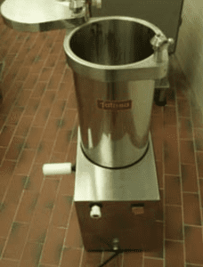 The side view of a silver automatic sausage stuffer on brick flooring against a white wall.