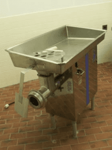 A silver meat grinder in a room with brick flooring and white walls