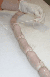 An individual wearing an orange shirt and white gloves using white string to tie off links of a sausage.