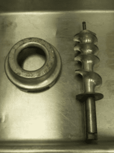 A silver metal screw auger and cap sitting on a metal surface.