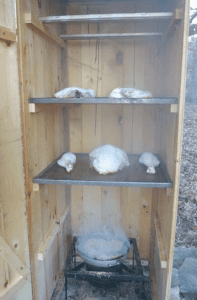 An open wooden smokehouse with meat cooking on trays
