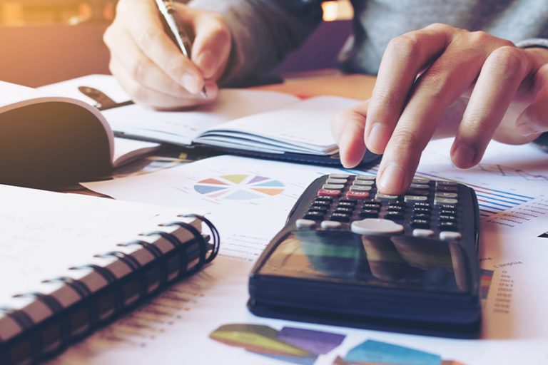 calculator and paperwork on a desk with a persons hand